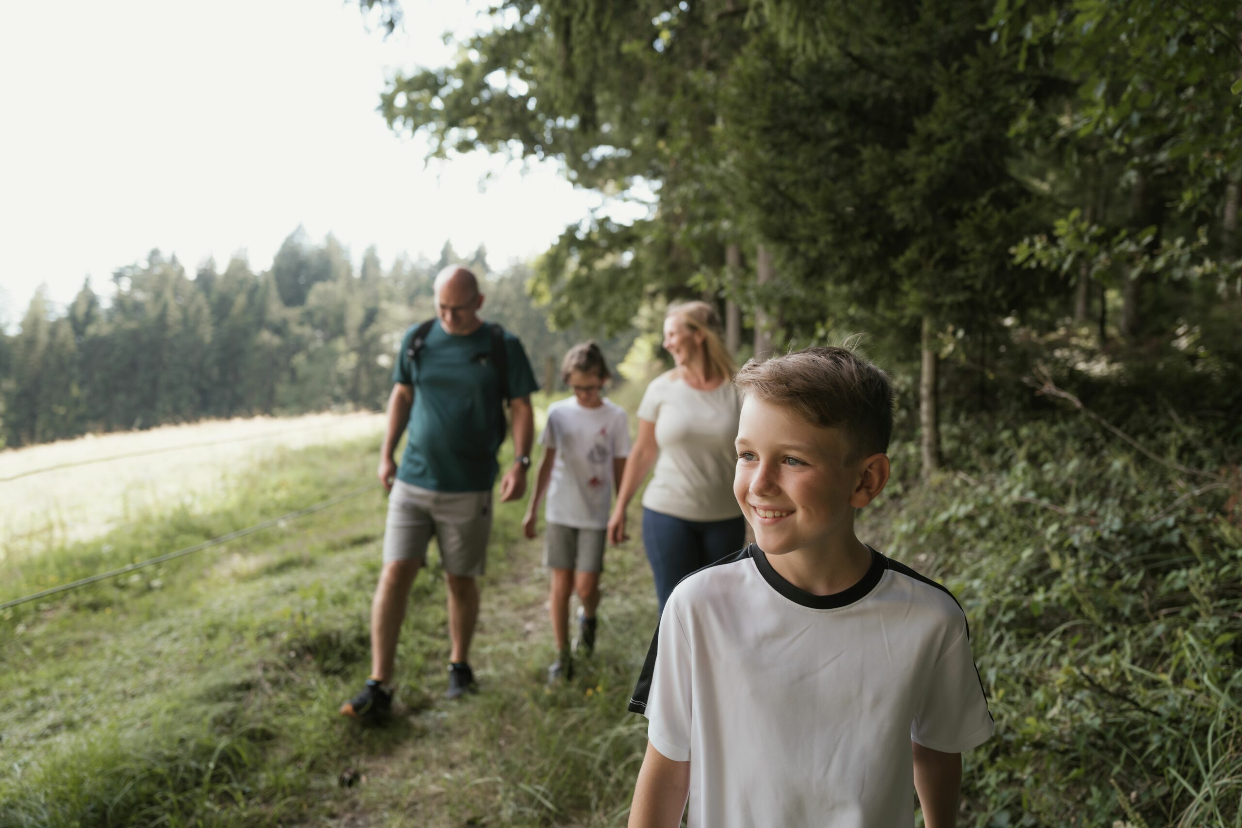 Eine Familie wandert auf einem Wiesenweg auf einer Waldlichtung, Foto: S´INNVIERTEL Tourismus_Matthias Klugsberger